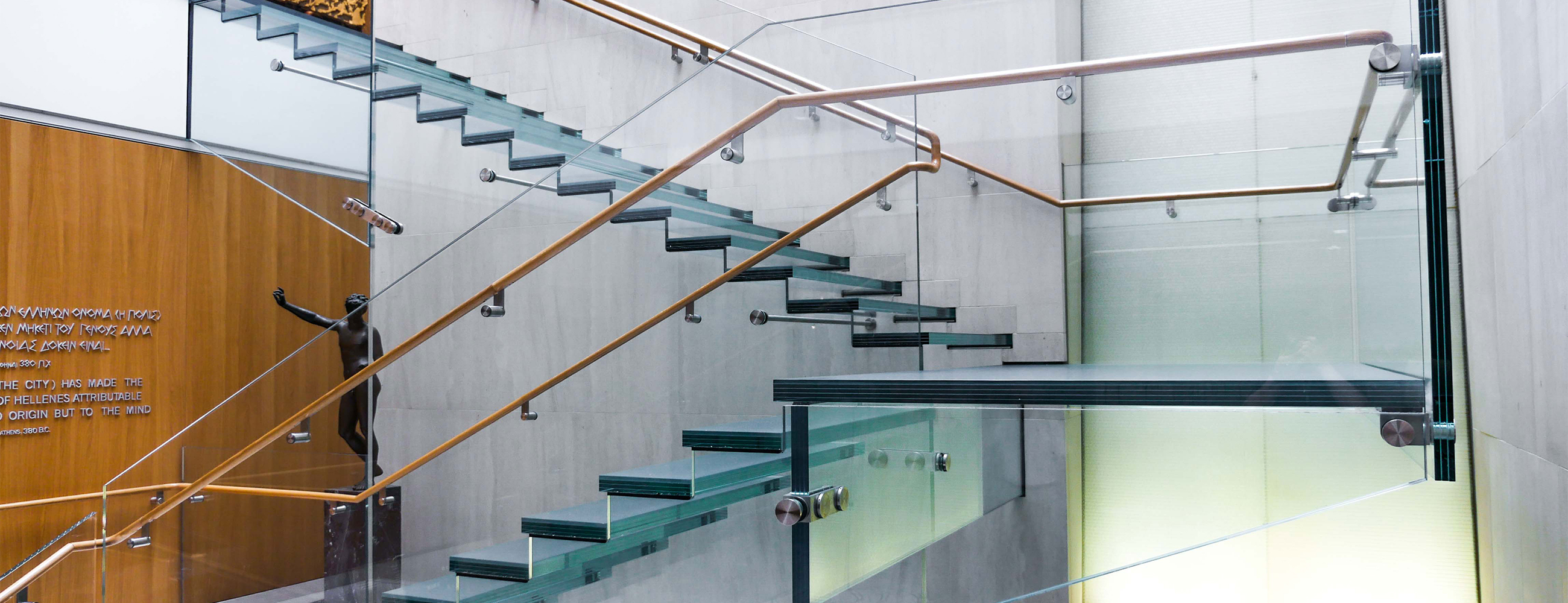 Side view of the all-glass staircase at the Onassis Cultural Center showcasing the stairs, ballustrades and railing.