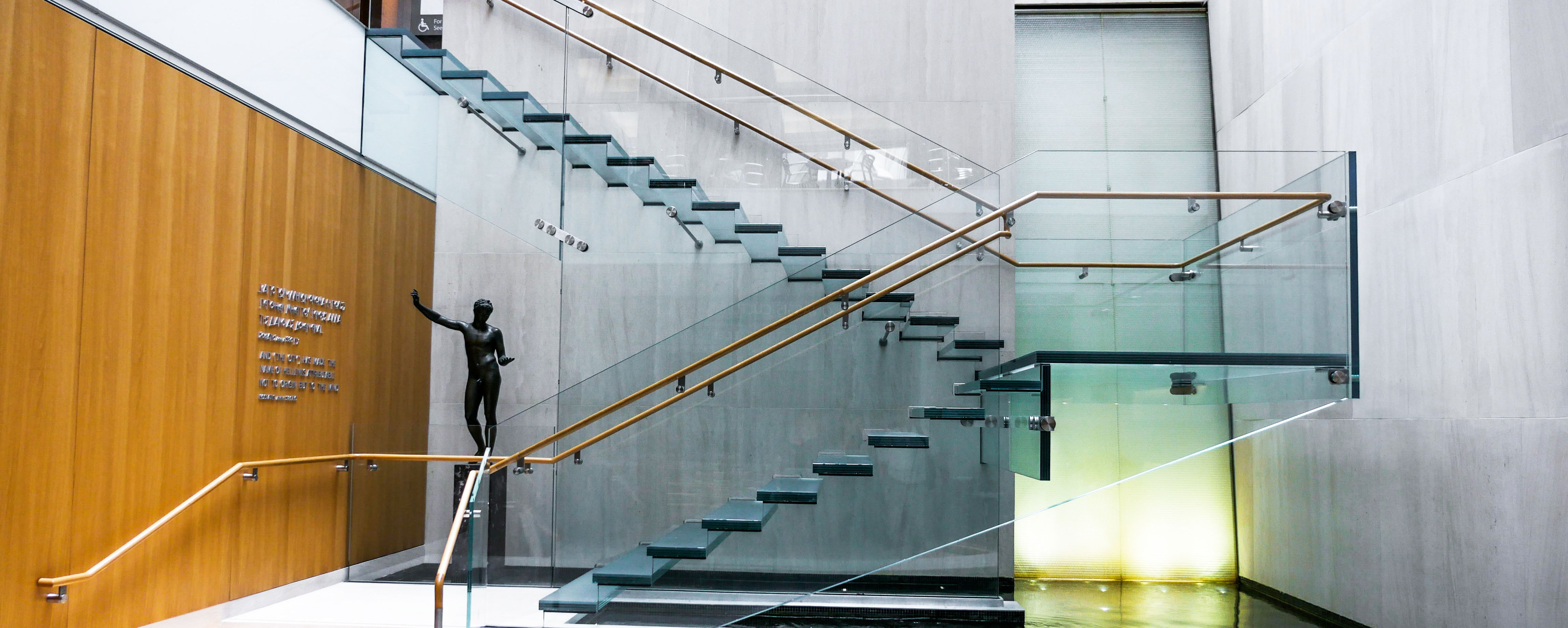 Side view of the all-glass staircase at the Onassis Cultural Center showcasing the stairs, ballustrades and railing.