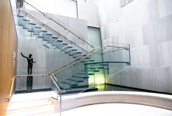 Side view of the all-glass staircase at the Onassis Cultural Center showcasing the stairs, ballustrades and railing.